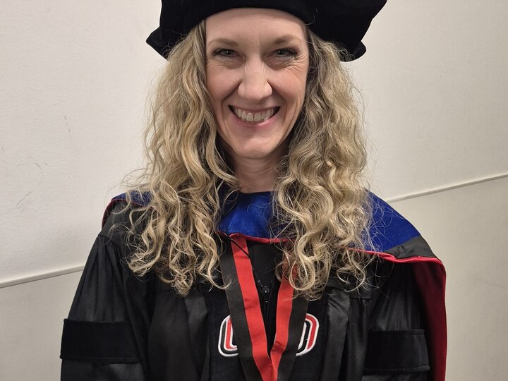 Graduate in black robe and cap with a medal on red ribbon.
