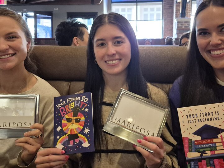 Three people holding graduation-themed gifts and cards while seated in a restaurant.